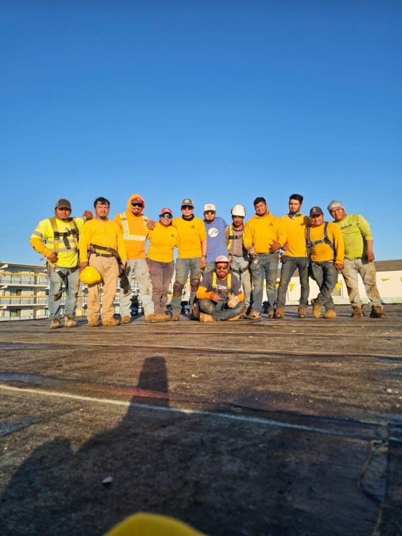 G and Bros Roofing Employees 109 Clark Street, Salisbury MD 21804 Commercial Roofing Contractor Residential Roofing Contractor 12 G and Bros Roofing employees posed to take a group picture on the roof of a job site. They are all wearing the G and Bros Roofing uniform and smiling.